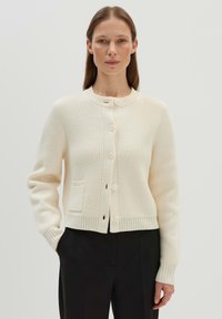 Cremefarbener Cardigan aus strukturiertem Strick, mit Rundhalsausschnitt, fünfknopfiger Verschluss und einer Fronttasche.