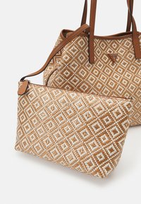 Geweven tas en pouch in een tan en witte geometrische patroon; heeft bruin leren accenten, dubbele banden en een ritsluiting op de pouch.