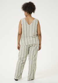 Gestreepte stof, bijpassende set van top en broek in crème met zwarte verticale strepen. Top heeft een V-hals aan de achterkant; de broek is wijduitlopend.