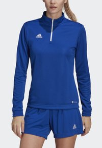 Top deportivo azul con un cuello alto y cierre de cuarto de cremallera, combinado con pantalones cortos a juego. Hecho de tejido suave y liviano con acentos del logo de Adidas.