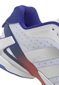 Scarpa sportiva bianca con accenti viola, tomaia in mesh, design strutturato, suola in gomma con dettagli rossi e blu e marchio ben visibile.