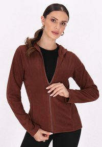Hanorac crem cu fermoar, confecționat dintr-un material moale, având glugă, mâneci lungi și un design ajustat, purtat peste un top negru.
