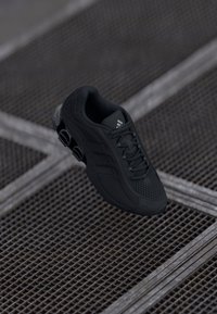 Zwarte sportieve schoen van mesh en synthetische materialen, met een gestructureerde bovenkant, zes rubberen dempelementen en vetersluiting.
