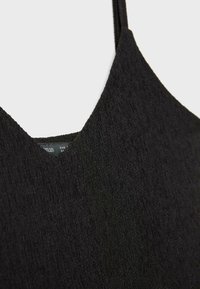 Crni top bez rukava s v-izrezom od teksturiranog materijala. Materijal ima rebrasti uzorak, naglašavajući čist, minimalistički dizajn.