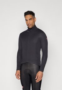 Maillot de cyclisme à manches longues en tissu noir avec col haut, coupe ajustée et poche zippée sur le côté. Texture lisse et design minimaliste.