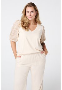 Beige V-hals top met gebreide kant pofmouwen, gecombineerd met lichtbeige broek met elastische tailleband en zijzakken. Glad textuur, comfortabele pasvorm.