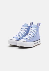 Tenisky s vysokým střihem v světle modré plátno s bílými tkaničkami, gumovou špičkou, černobílým pruhovaným středním podešvem a texturovanou podrážkou.