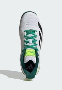 Scarpa sportiva bianca con lacci verdi, accenti verdi e neri, strisce Adidas nere sui lati e etichetta gialla neon sulla linguetta.