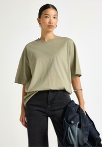 Olivgrön bomullsoversized t-shirt med korta ärmar, rund halsringning, ihopparad med högmidjade mörka jeans och en denimjacka.