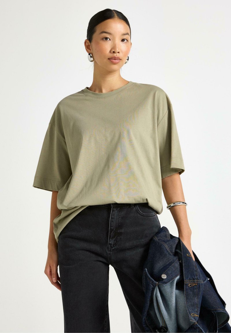 Olivgrön bomullsoversized t-shirt med korta ärmar, rund halsringning, ihopparad med högmidjade mörka jeans och en denimjacka.
