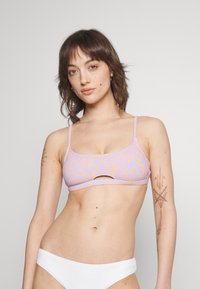 Lila bikiniöverdel med ett orange blommönster, med tunna axelband och ett utskuret mittparti. Texturerad tyg och matchande vita underdelar.