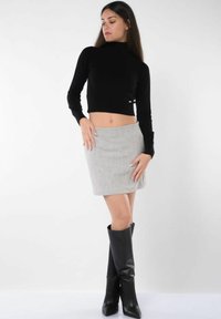 Maglione cropped nero con collo alto abbinato a una mini gonna grigia e stivali neri al ginocchio. Tessuti morbidi e design aderente in tutto.