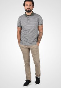 Polo tričko so sivými a bielymi pruhmi, tmavozeleným golierom, v kombinácii s béžovými nohavicami a čiernymi teniskami. Má slim fit strih.