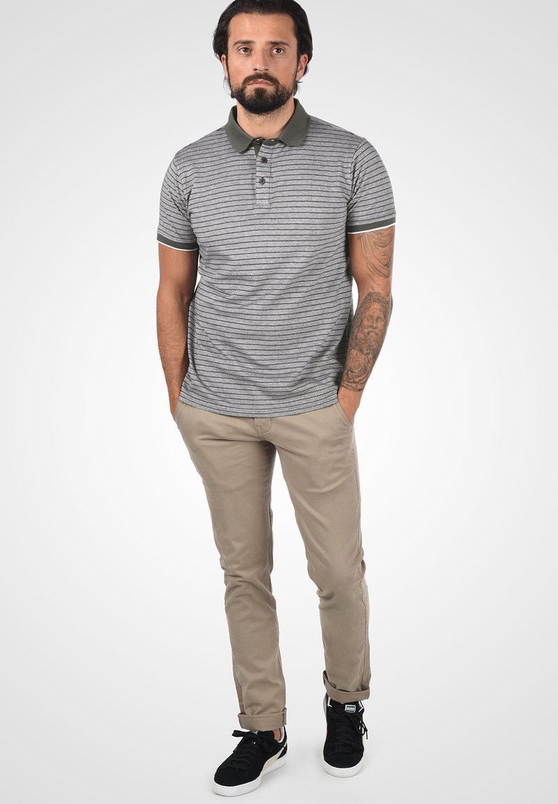 Polo tričko so sivými a bielymi pruhmi, tmavozeleným golierom, v kombinácii s béžovými nohavicami a čiernymi teniskami. Má slim fit strih.