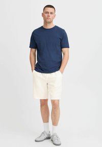 Navy blue cotton t-shirt, short sleeves; cream shorts in lightweight fabric with an elastic waistband; gray sneakers and white socks.