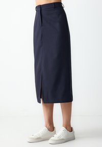 Marineblauwe gestreepte midi-rok met een voorkleur, voorzien van een tailleband met riemlussen. Gepaard met witte sneakers. Zachte stofstructuur.