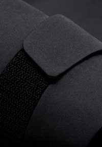 Tessuto nero caratterizzato da una superficie liscia e un accento nero intrecciato. Include una patta rettangolare con angoli arrotondati in alto a sinistra.