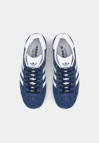 Adidas sneakers med ovandel i marinblå mocka, vita läderdetaljer, tre ränder och mörka snören. Platt gummisul, rund tådesign.