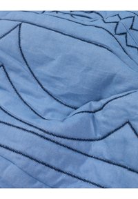 Blauer Stoff mit Zickzack- und geraden schwarzen Stichmustern, die geometrische Formen und Linien auf einer weichen, zerknitterten Oberfläche schaffen.