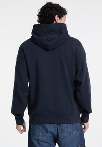 Sudadera con capucha azul marino que presenta un corte relajado, puños y dobladillo acanalados. Fabricada con una tela suave de textura lisa.