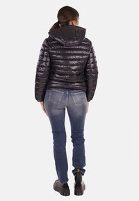 Giubbotto a sacco nero con design a righe orizzontali, cappuccio attaccato e finitura lucida. Abbinato a jeans aderenti blu e stivali neri.
