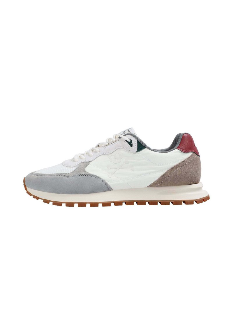 Zapatilla blanca, gris y beige con lengüeta trasera roja, logo de calavera y huesos cruzados en el costado, suela texturizada y cierre de cordones.