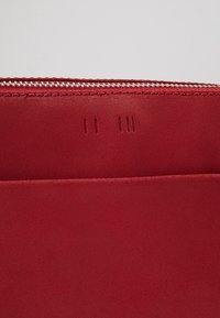 Punainen nahkalompakko, jossa on sileä pinta, vetoketjukiinnitys ja pystysuorat ompelusaumat. Ulkopuolella korttipaikat.