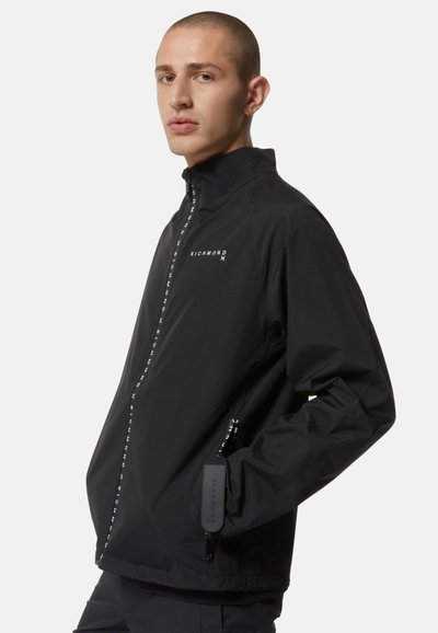 Giacca leggera nera con colletto alto, chiusura con zip sul davanti e polsini elastici. Presenta il nome del marchio stampato lungo la zip e sul lato.