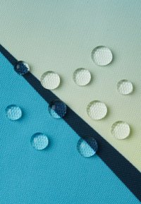 Krople wody zbierające się na powierzchni tkaniny podzielonej czarną linią, z jednej strony w jasnym niebieskim kolorze, a z drugiej w jasnoszarym.