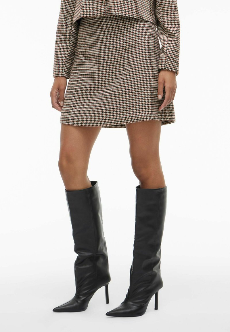 Mini suknja smeđe boje s uzorkom ptičje kosti i uskim krojem, uparena s crnim kožnim čizmama na visoku petu do koljena.