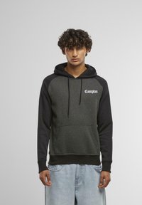 Sweatshirt à capuche noir et gris foncé avec une poche avant, affichant "Compton" en écriture blanche sur la poitrine et des manches contrastantes.