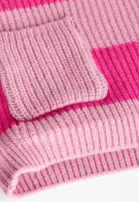 Stickad tröja i nyanser av rosa, med en ribbad textur, en fyrkantig ficka och en djärv randig design. Mjuk och tjockt tyg.