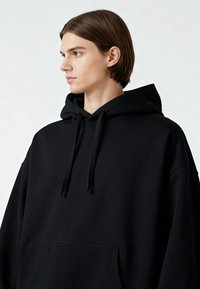 Sudadera negra con capucha ajustable, corte oversized y bolsillo frontal. Fabricada con una tela suave de textura lisa.