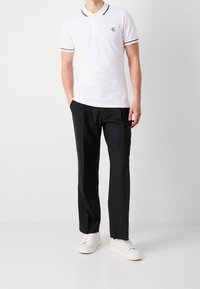 Vit polo shirt med svart trim och logotyp, matchad med svarta byxor och vita sneakers. Slät tyg och klassisk passform.