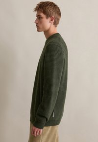 Grüner strukturierten Strickpullover mit Rundhalsausschnitt und gerippten Akzenten, ausgestattet mit langen Ärmeln und einem entspannten Schnitt.