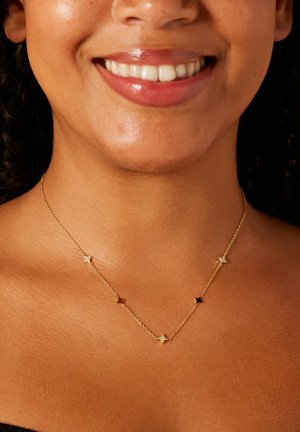 Collier en chaîne dorée présentant des accents alternés en forme d'étoile et ronds, avec des finitions mates et brillantes. Détails ornés de petits pierres précieuses.