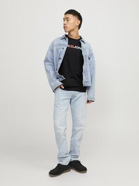 Lichtblauwe spijkerjasje over een zwart t-shirt met witte tekst; gecombineerd met lichtgewassen jeans en zwarte schoenen met een gestructureerde zool.
