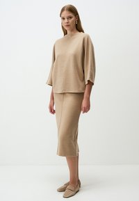 Beige Strickoberteil mit weiten Ärmeln und hohem Ausschnitt, kombiniert mit einem knielangen, taillierten Rock, beide mit einer glatten Textur.