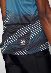 Lyhythihainen urheilupaita sinivihreänä ja mustana, geometrisilla kuvioilla ja valkoisilla raidoilla, jossa on logo helmassa. Kapean leikkauksen malli.