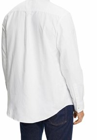 Weißes Langarm-Hemd mit Knopfleiste und spitzen Kragen, Rückeneinsatz und knöpfbaren Manschetten, kombiniert mit dunklen Denim-Jeans.
