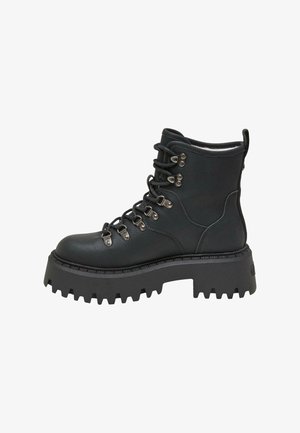 Personne sortant d’un véhicule portant des bottes noires épaisses à lacets, une jupe à carreaux et un trench-coat sombre sur un trottoir urbain ensoleillé.