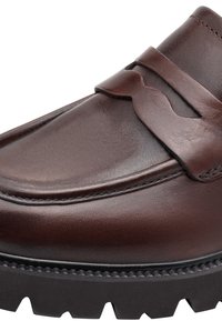 Gros plan sur un mocassin en cuir marron foncé avec une bride à penny et une semelle en caoutchouc noire texturée.