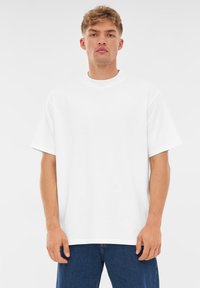 Vit bomulls t-shirt med rund halsringning och korta ärmar, med avslappnad passform och enkel design. Bärs med blå jeans.