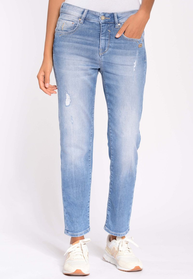 Vaqueros de mezclilla azul claro con ajuste slim, con detalles desgastados y una cinturilla estándar. Estilizados con zapatillas blancas.