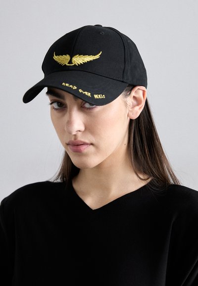 Sort kasket med et gyldent vingeemblem foran og "HEAD OVER HEELS" broderet i gult på skyggen. Fremstillet af struktureret stof.