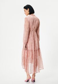 Lange, roze doorschijnende jurk met een geplooide taille, gelaagde zoom en een subtiel gespikkeld patroon. Gestyled met roze hoge hakken.