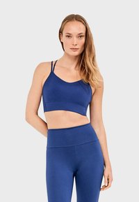 Sujetador deportivo de tela azul intenso con tirantes finos y ajustables, con escote redondo y textura lisa y sin costuras. Leggings a juego de talle alto.
