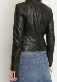 Svart skinnjacka med en figursydd design, dragkedja vid ärmsluten och subtila sömmandetaljer, kombinerad med en blå jeanskjol i A-linjeform.