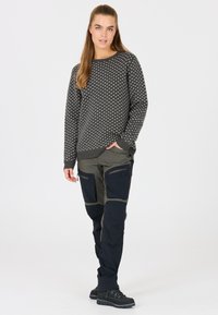 Grauer Pullover mit weißem Muster, kombiniert mit olivgrünen und marineblauen Cargo-Hosen mit Reißverschlusstaschen. Schwarze feste Schuhe vervollständigen das Outfit.