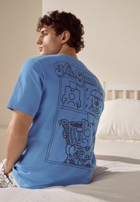 Ljusblå bomull t-shirt med en svart linje-grafiktryck av tecken och text på baksidan, som refererar till "Mr. Grumpy."